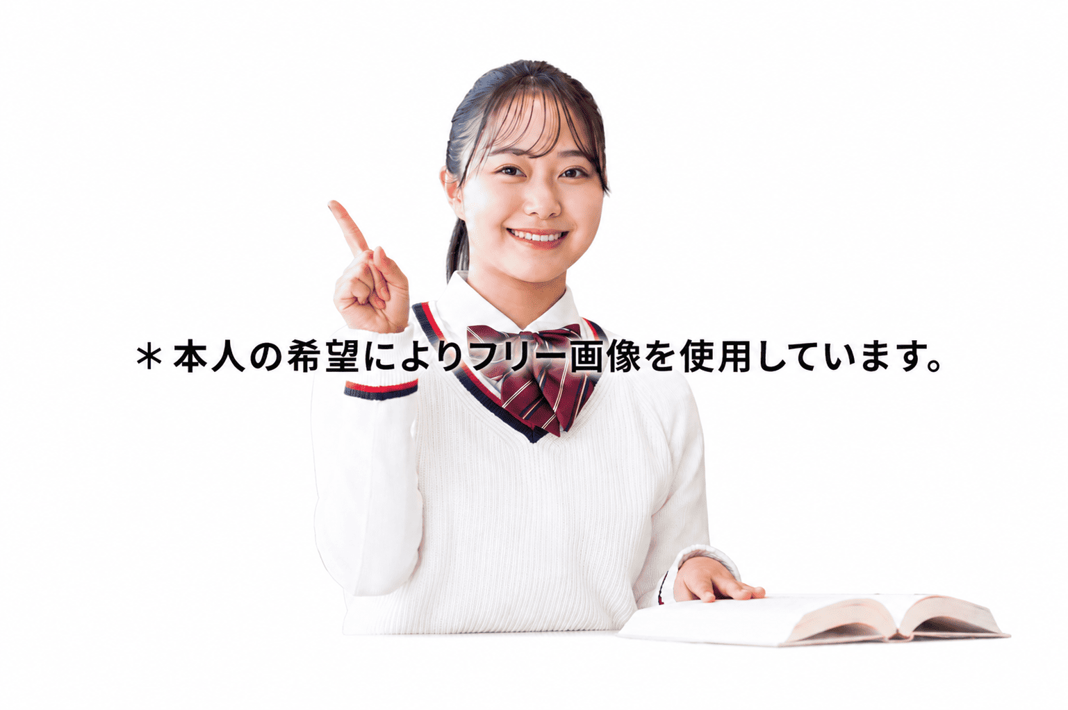 Smiling Japanese student in a white sweater and bow, pointing upward, with a book open on the desk and Japanese text across the image indicating a free stock photo used by request of the person.