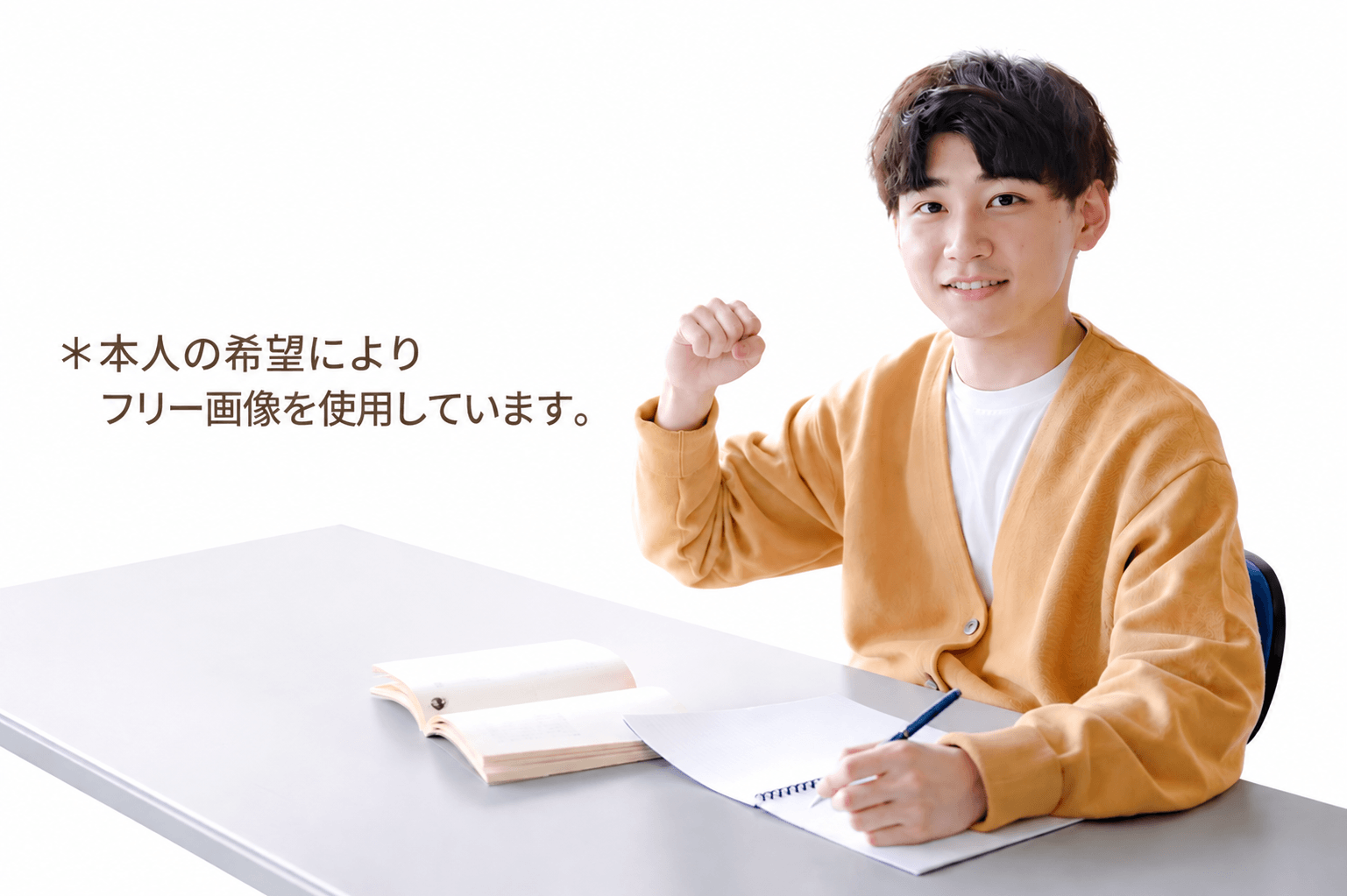 Young man at a desk with an open book and notebook, smiling and raising a fist in a gesture of encouragement.